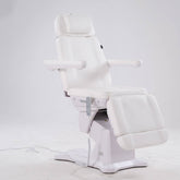 A white adjustable spa or treatment chair with padded headrest, armrests, and a reclining footrest, shown on a light gray studio background.